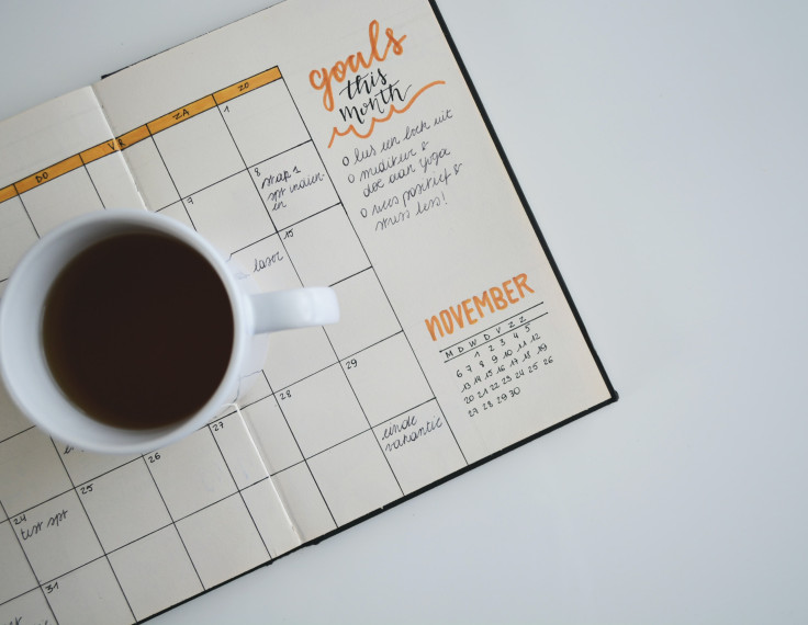 Cup of coffee sitting on top of an open planner with goals for the month outlined