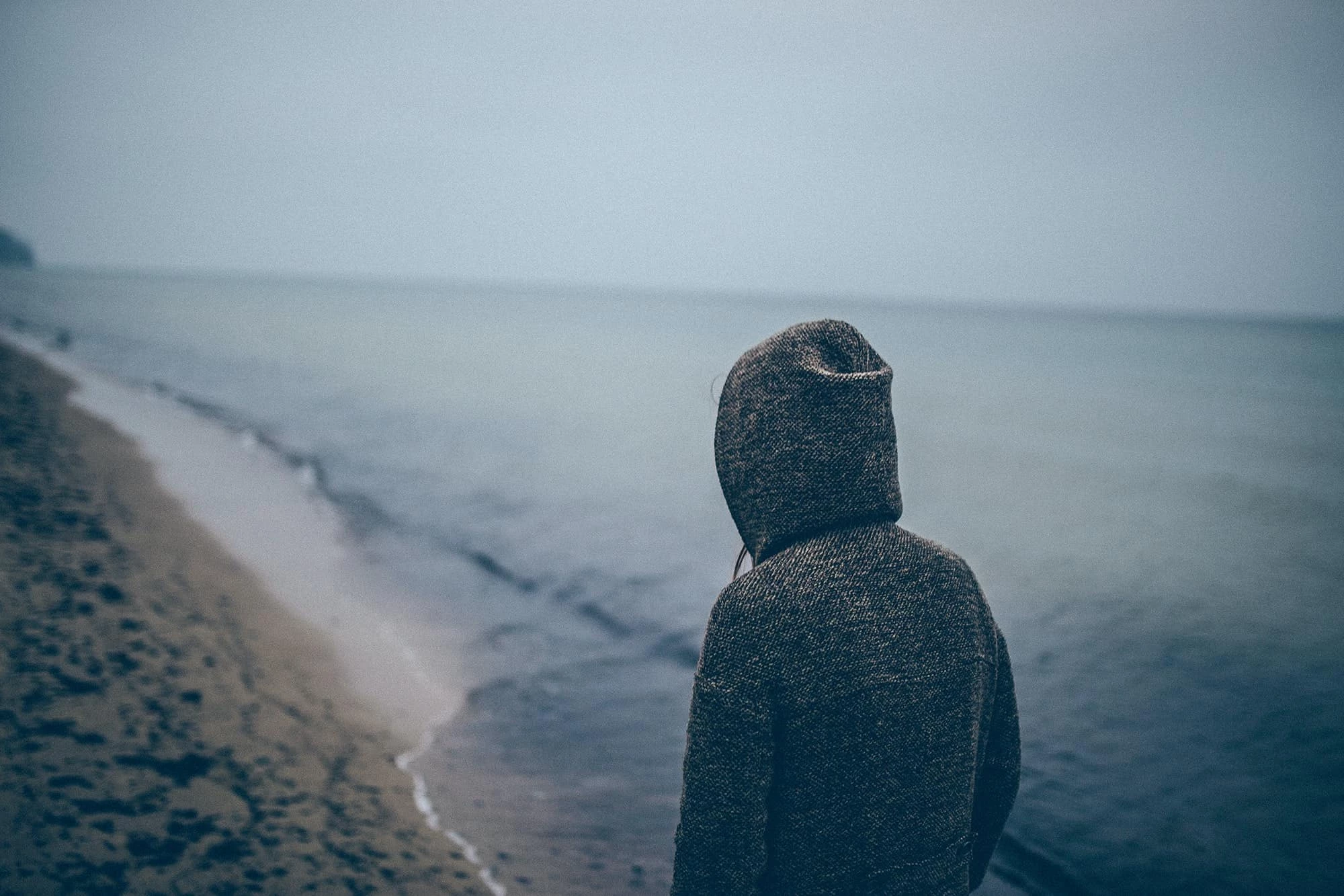 Person in hoody looking down a moody coastline