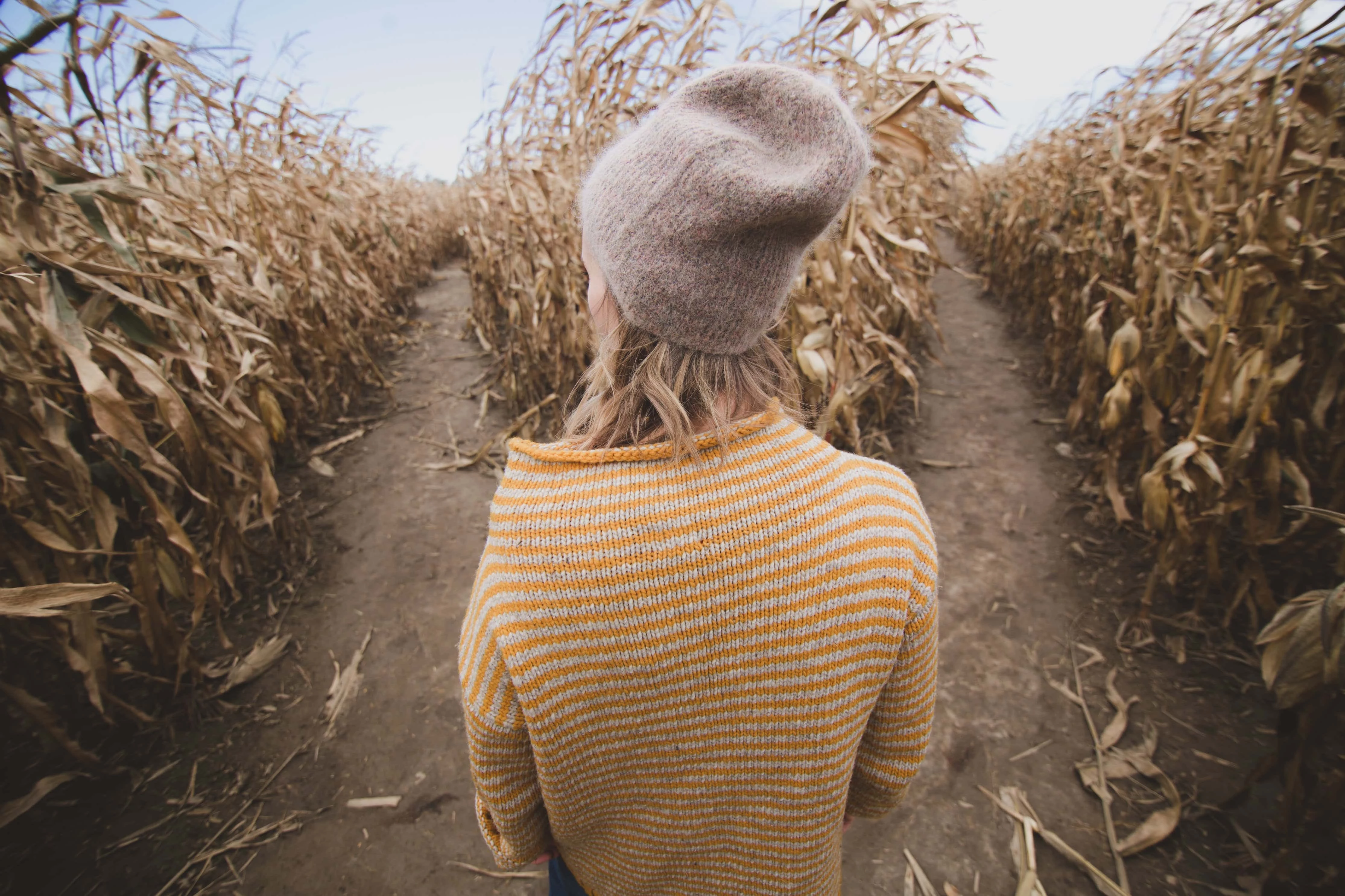Woman in woollen hat standing at fork in a corn maze
