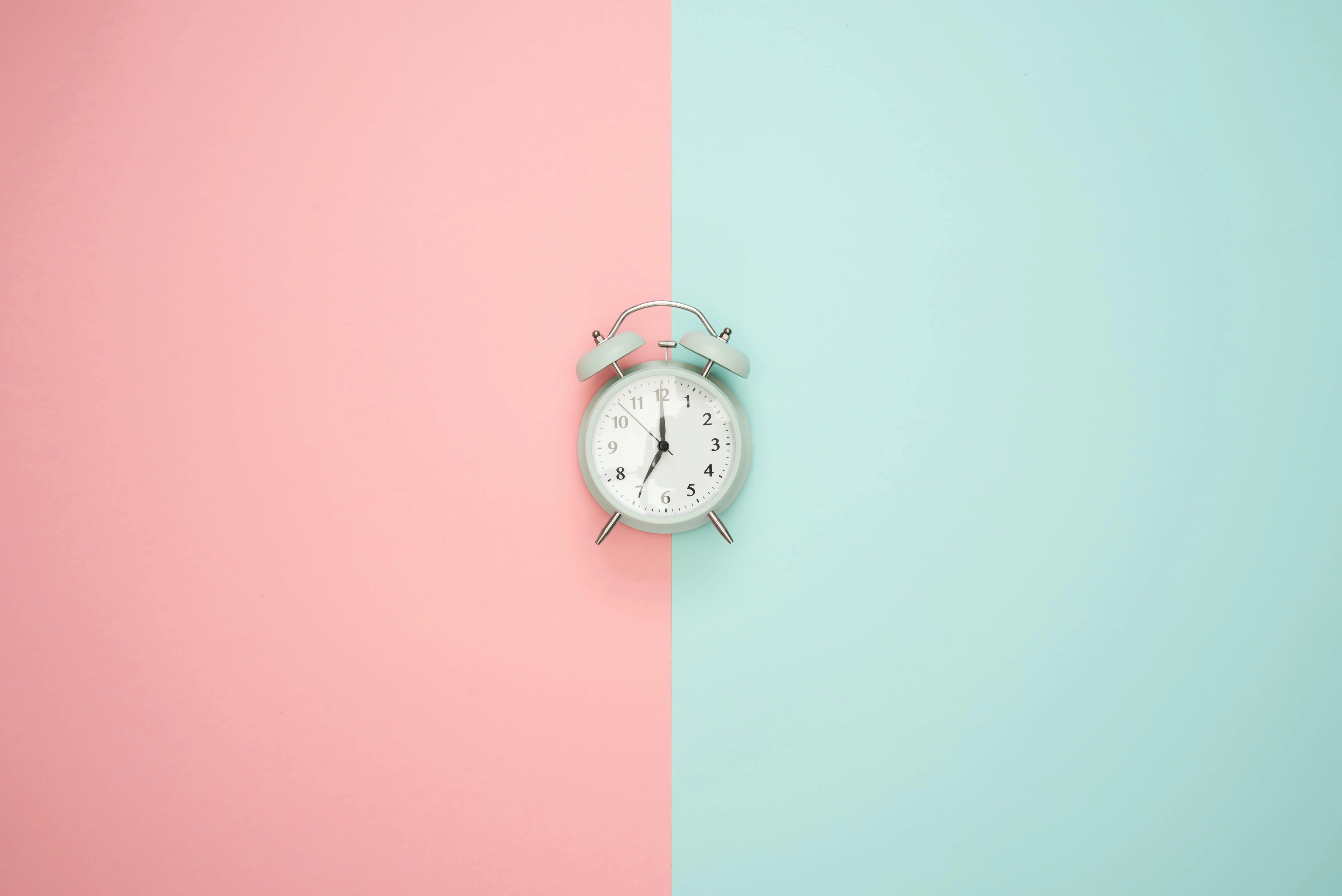 Old-fashioned clock in front of pale pink and pale blue background